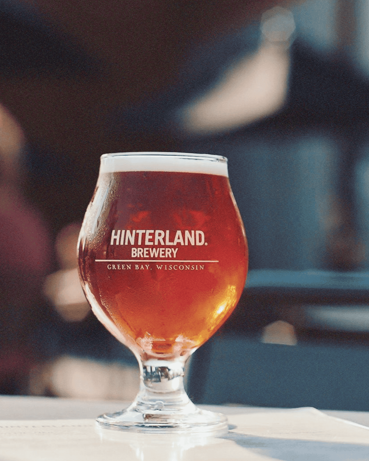 A goblet glass full of amber-colored beer that says Hinterland Brewery, Green Bay, Wisconsin on it sitting outside.