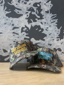 Two camouflage hats embroidered with the words "Hinterland Brewery."