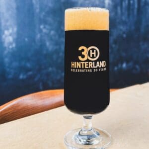 A picture of the Hinterland 30th anniversary glass - a slender, kolsch-looking glass but with a short stem that has the Hinterland 30th anniversary logo in gold ink.