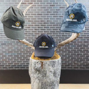 Three KUHL brand outdoor hats embroidered with the Hinterland logo in different colors - Greyish-Olive, Grey, and Grey Camo.