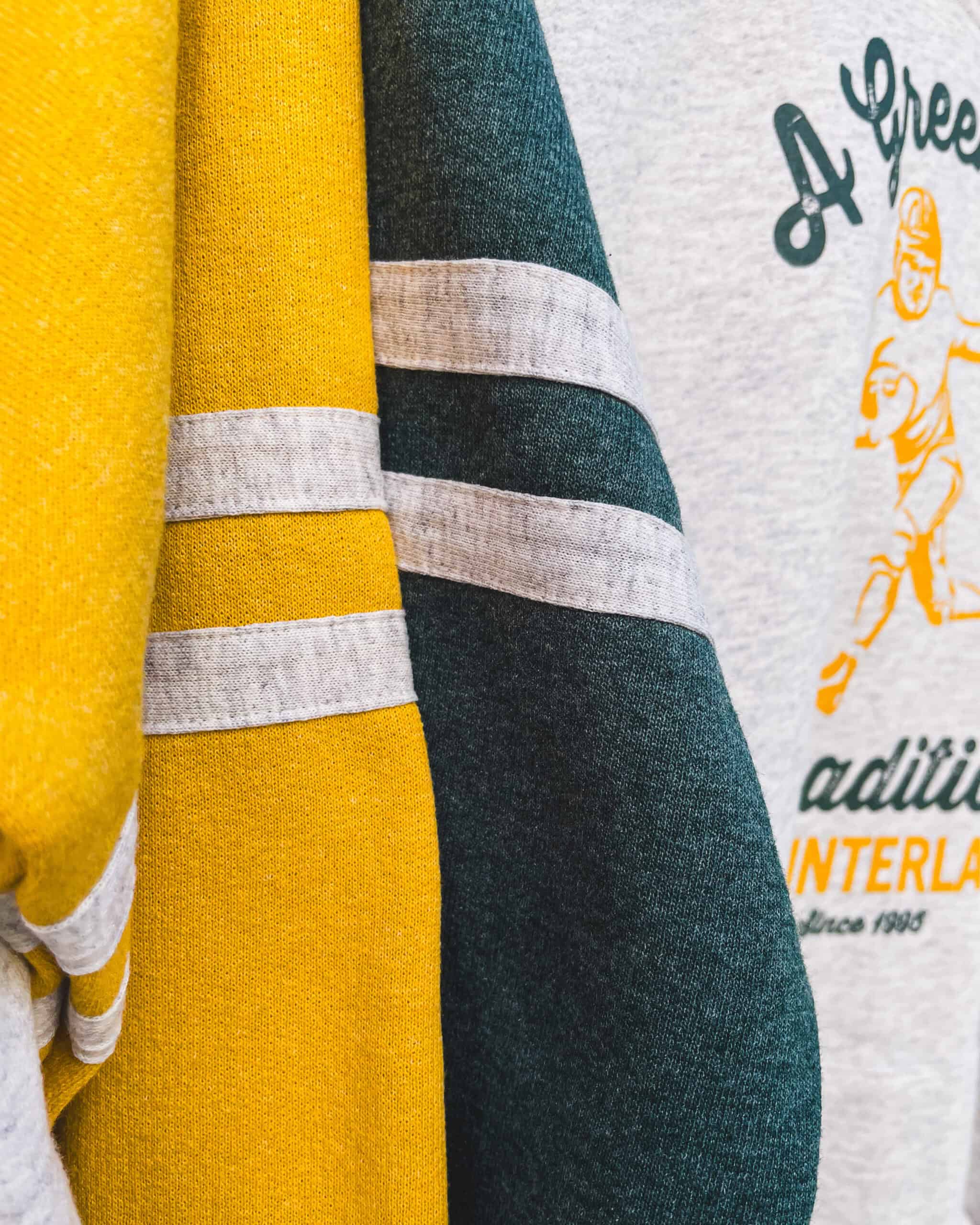 A close up of two sweatshirt sleeves, one in green and one in yellow. They both have athletic varsity stripes on them.