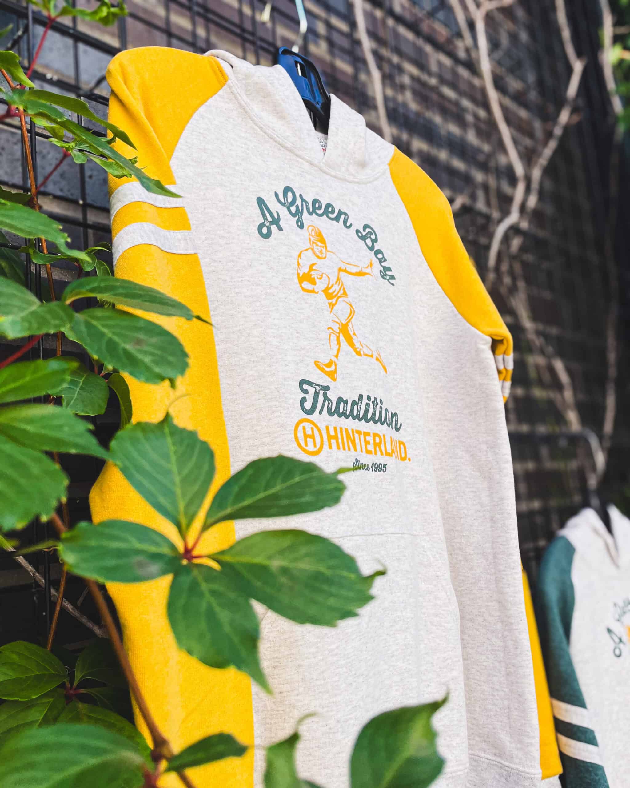 A pullover hoodie with yellow sleeves hanging on a fence. The sweatshirt has an image of a retro looking football player on it.
