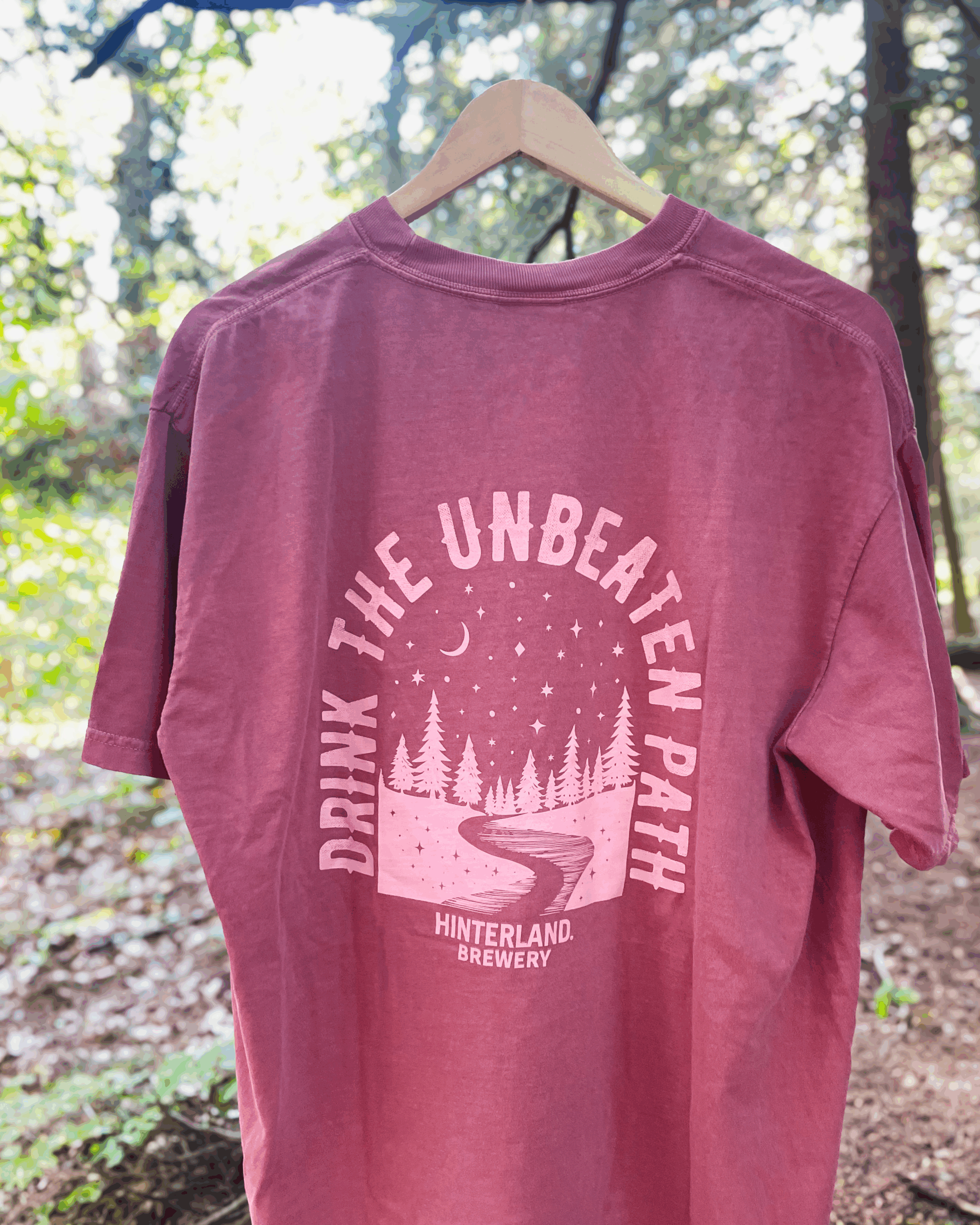 Red shirt hanging in the woods, on the back it says drink the unbeaten path, Hinterland Brewery.